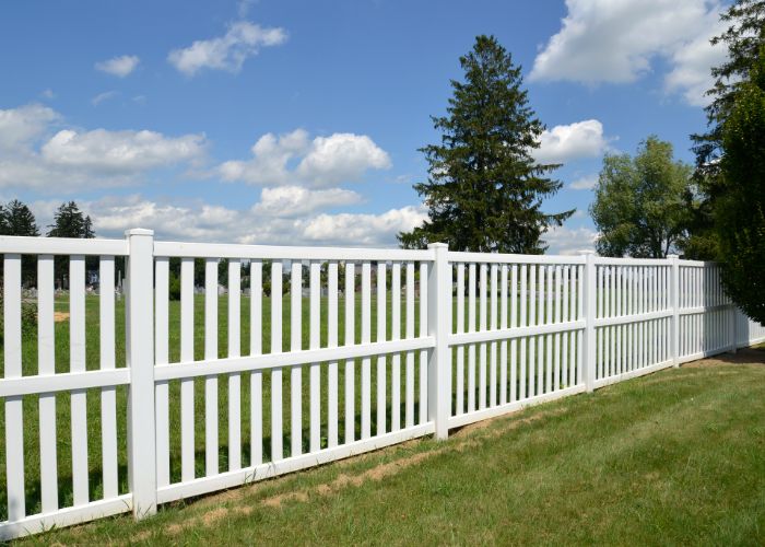 White vinyl fence bordering a grassy yard on a clear day during a fence replacement attleboro project.